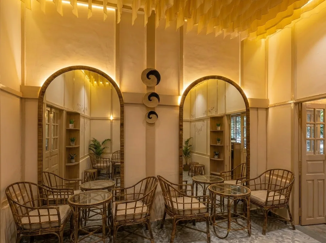 The mirrored double-arch accent wall beside the tea bar, with rattan armchairs and glass-top tables either side